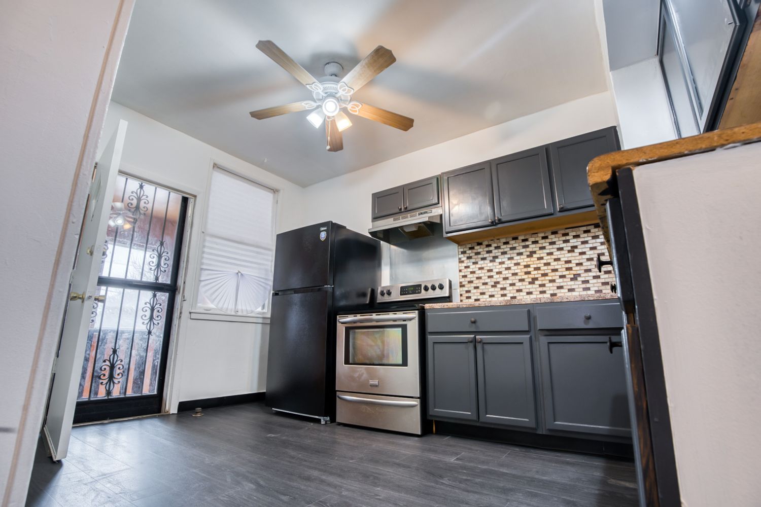Open concept apartment interior with ceiling fan and modern black kitchen cabinets.