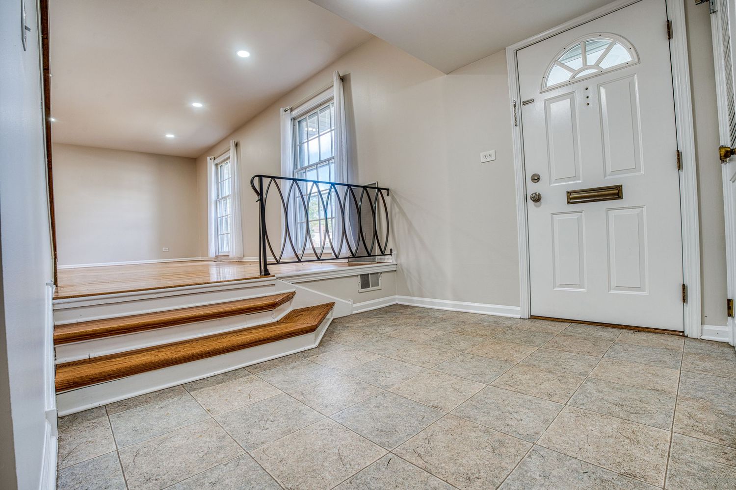 Bright basement entryway with beige tile flooring and white walls leading to wooden stairs.