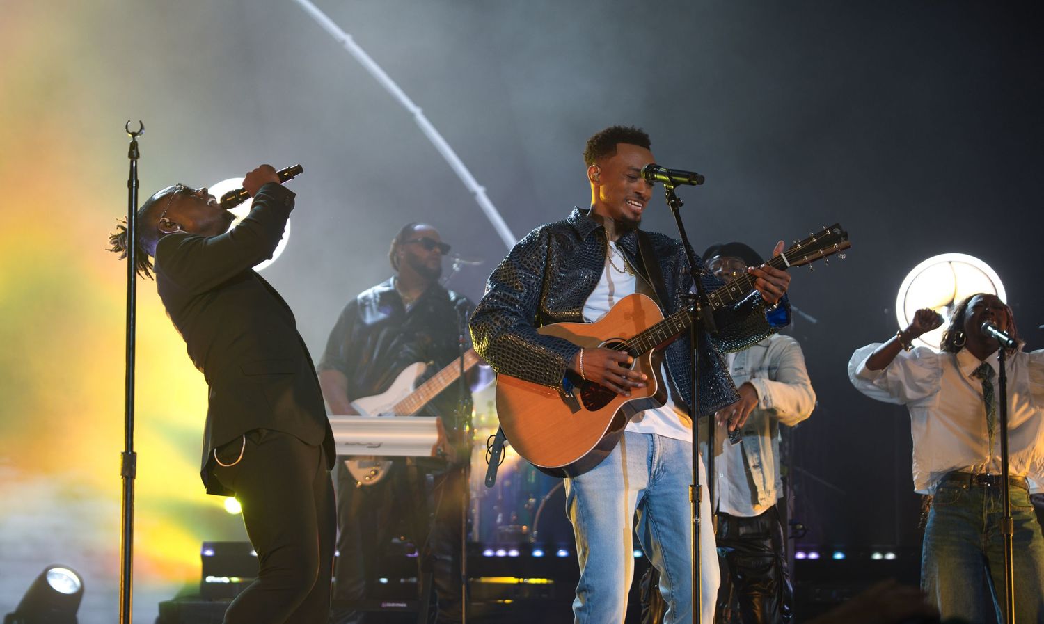 Musicians performing on dimly lit concert stage with spotlights and instruments.