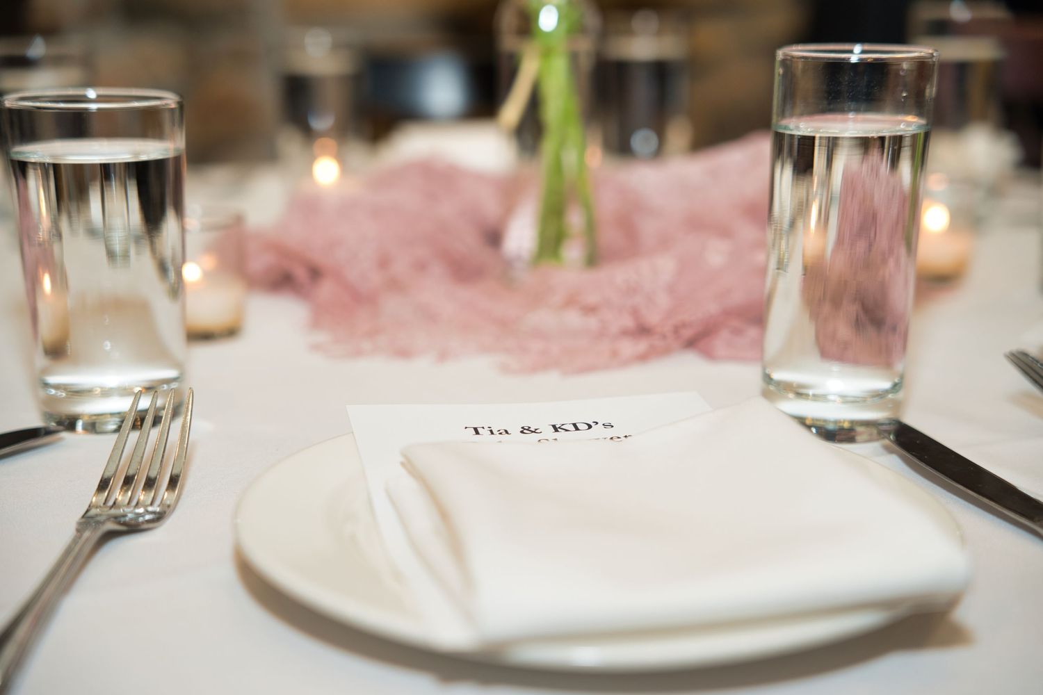 A table setting at an elegant restaurant with white plates, glassware, and soft pink ambient lighting.