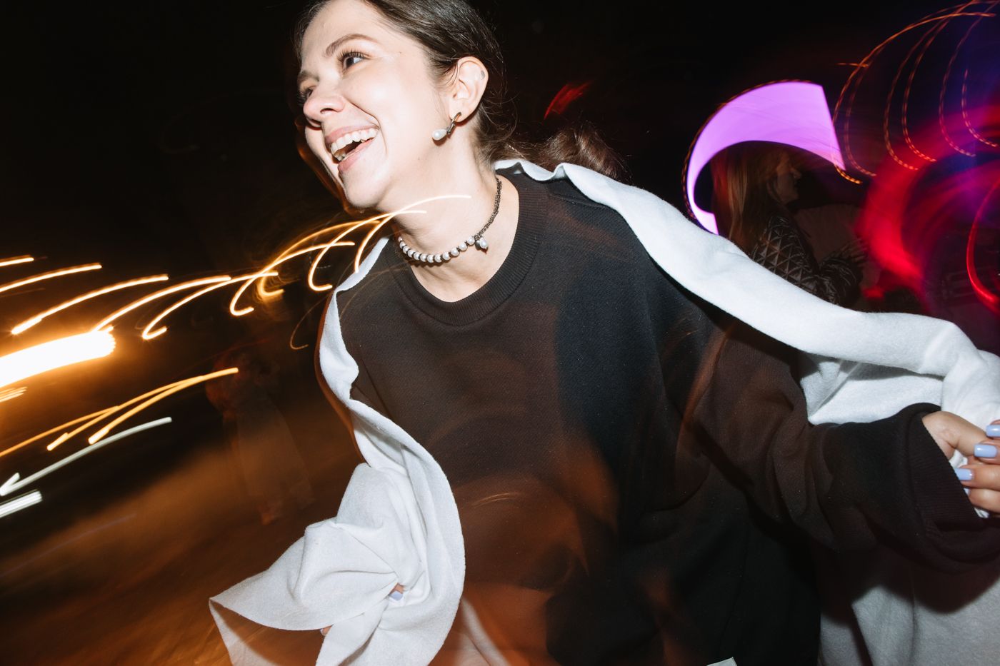 Dancers in white dresses twirl and move energetically on a dark dance floor with colorful lighting effects.