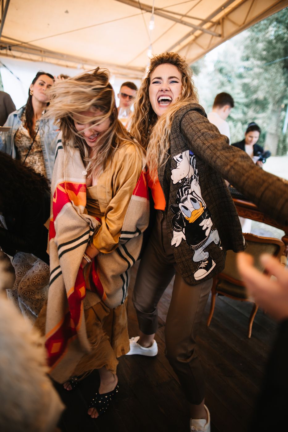 People dancing energetically under a white tent at an outdoor party with hair flying and bodies moving to the music.