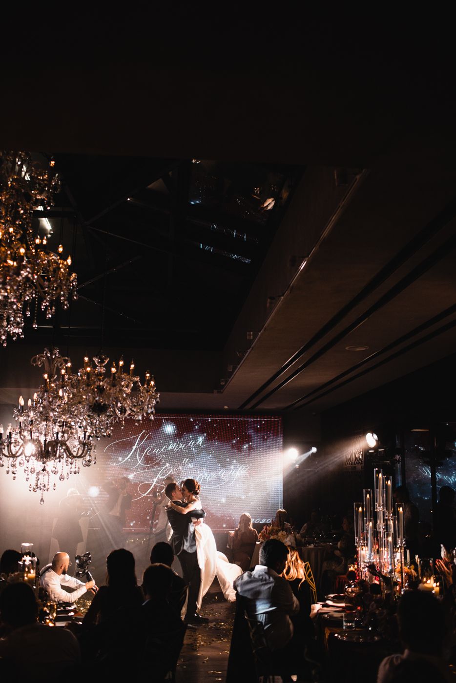 Wedding reception venue with crystal chandeliers and atmospheric lighting.