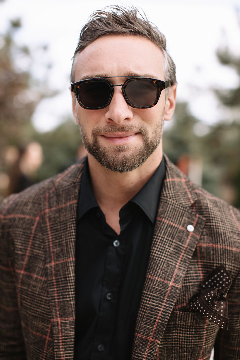 Stylish man wearing plaid blazer, black shirt and sunglasses outdoors.