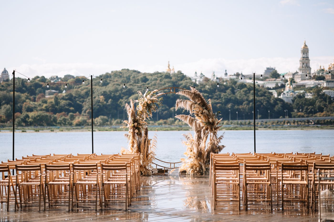 Wooden chairs arranged in rows for an outdoor waterfront ceremony with a scenic lake and trees in the background.