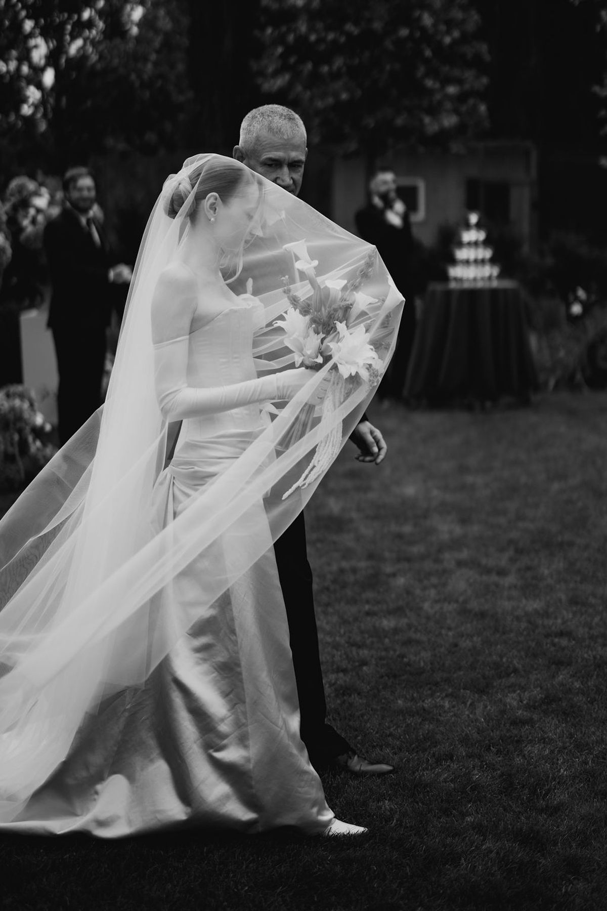 A flowing white wedding veil billows dramatically in the wind during an outdoor wedding photoshoot.