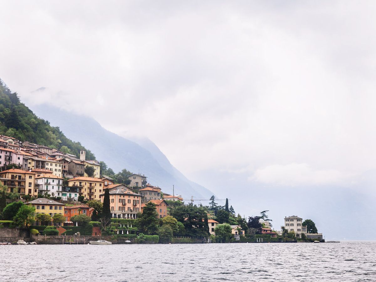 Scenic view of colorful buildings nestled on hillside along Lake Como in Italy with misty mountains in background.