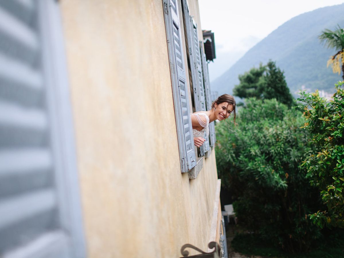 A rustic cream-colored wall with blue shutters and lush green foliage in the background.
