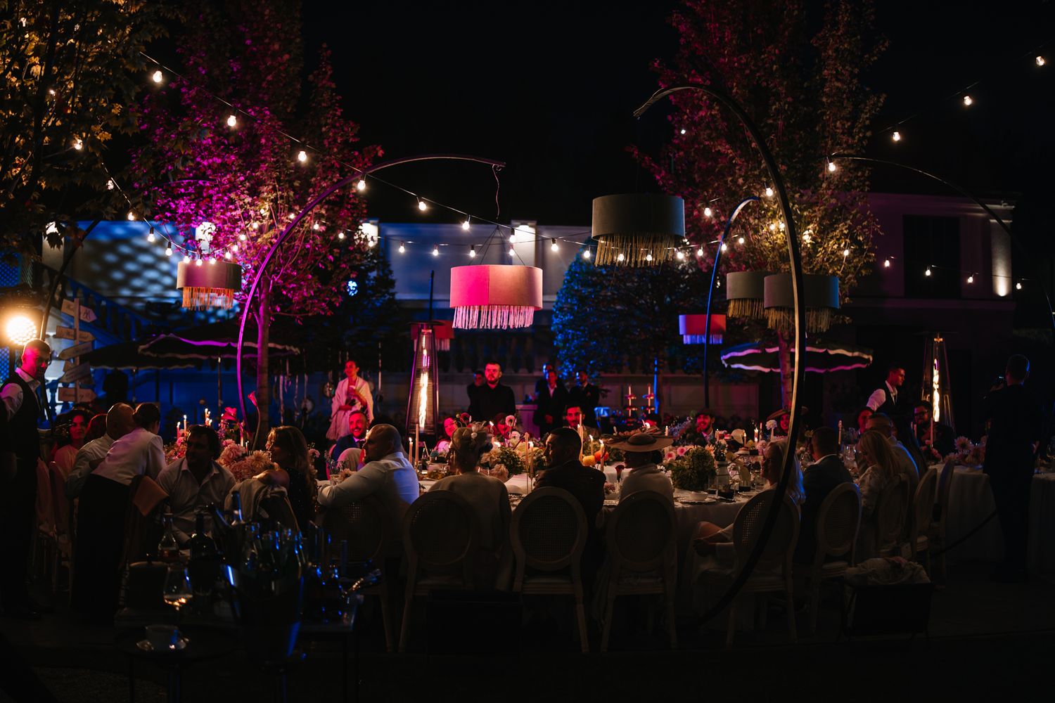 Colorful lights illuminate an outdoor nighttime festival scene with people enjoying entertainment and festivities.