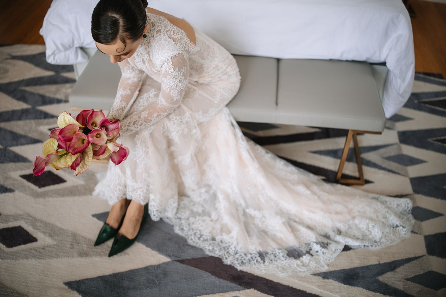 A bride in a flowing lace wedding dress sits gracefully on a patterned marble floor.