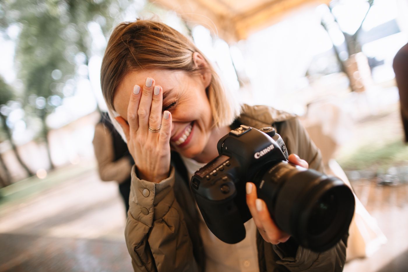 A photographer laughs while holding a professional camera with telephoto lens outdoors.