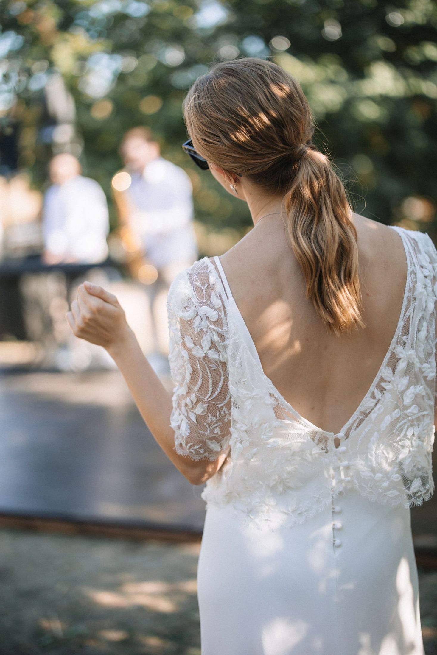 Close-up view of a delicate white lace wedding dress with intricate floral details shown from different angles in natural light.