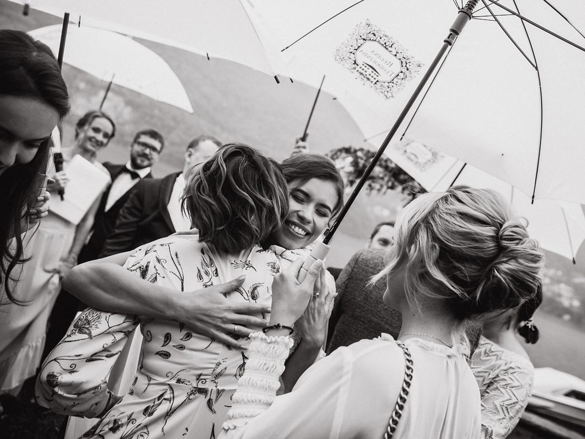 A joyful group gathers under a white umbrella at an outdoor celebration, sharing laughter and embraces.