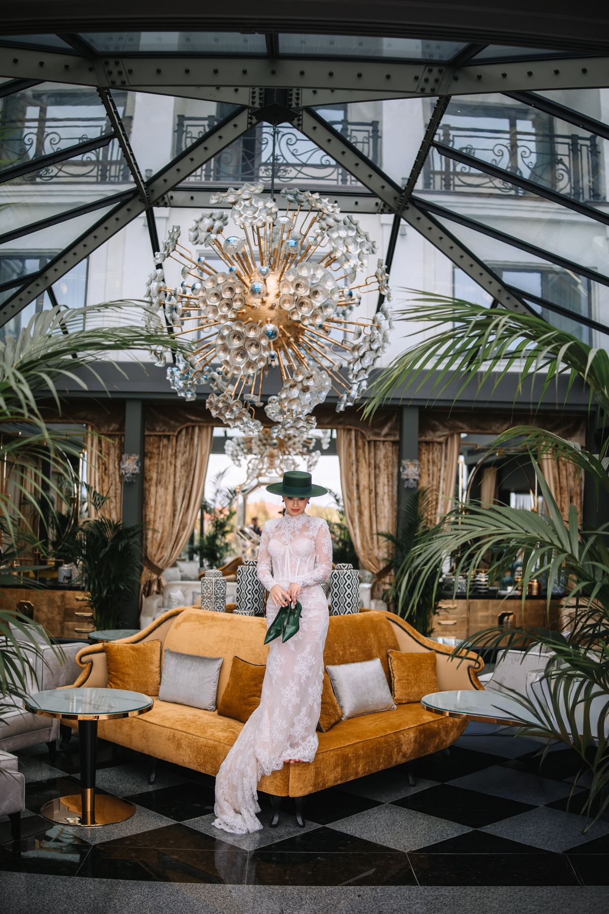 A luxurious greenhouse lounge with velvet orange couches, tropical plants, and crystal chandeliers creates an elegant atmosphere.