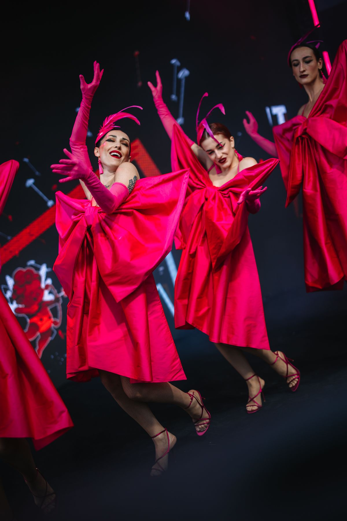Dancers in flowing red dresses leap gracefully through the air during a dynamic stage performance.