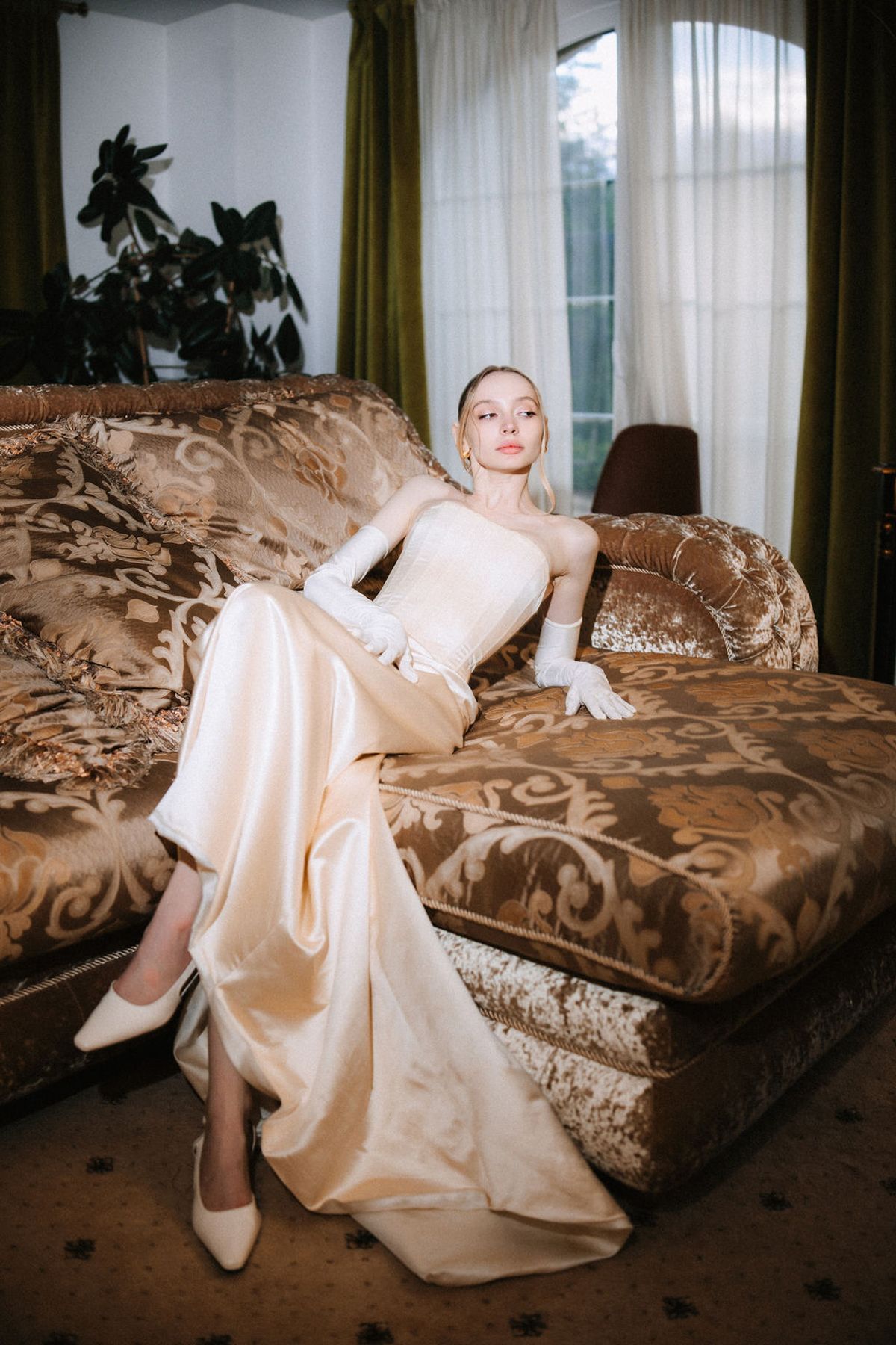 A vintage-inspired fashion photo featuring an elegant cream gown on a brown velvet couch with ornate patterns.