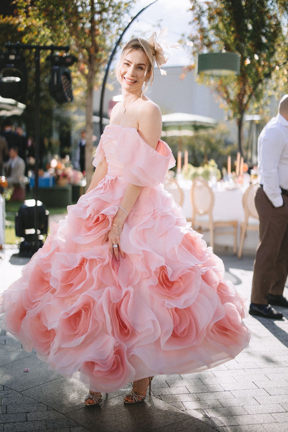 A flowing pink ruffled ballgown dress twirls gracefully in an outdoor setting with trees and sunlight.