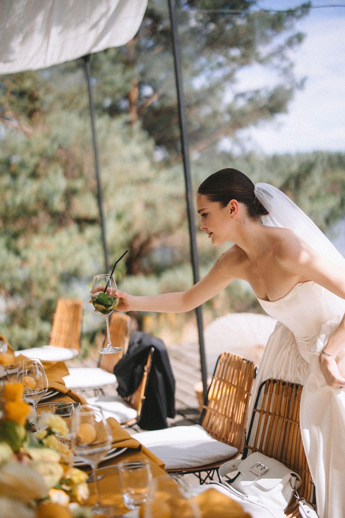 A person in a white wedding dress reaches across an outdoor table decorated for a reception.
