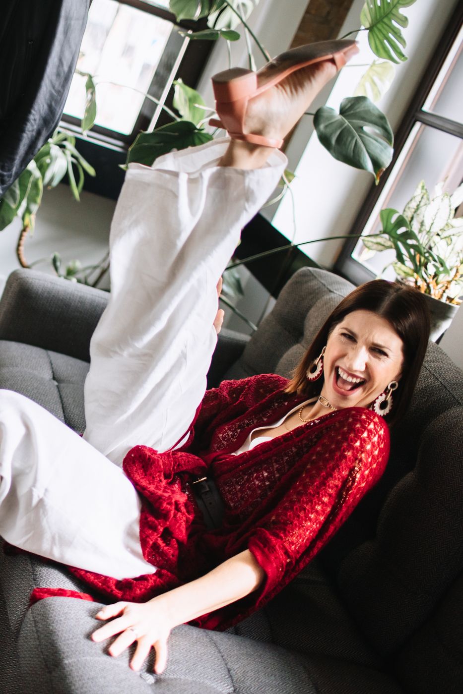 A sequence of photos showing someone in a red dress lounging playfully on a dark couch with indoor plants in the background.