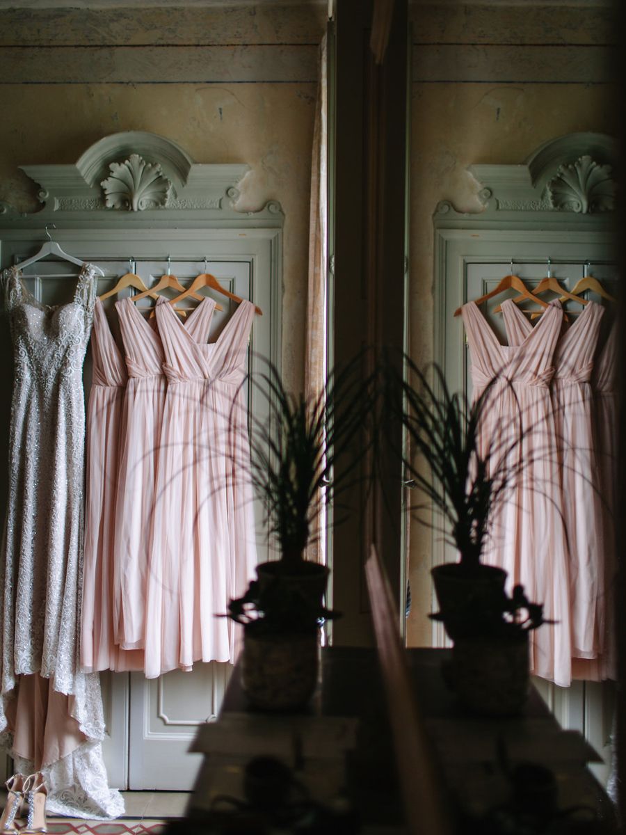Pink and white vintage dresses hanging in a row on ornate wall hooks beneath decorative molding and candle sconces.