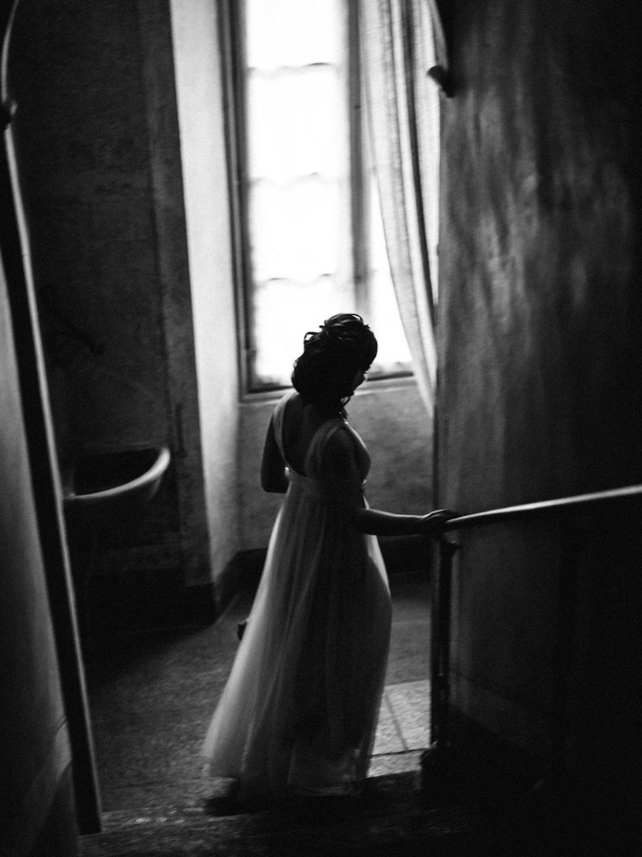 Silhouetted figures in a moody black and white wedding scene with dramatic window lighting and flowing dress.