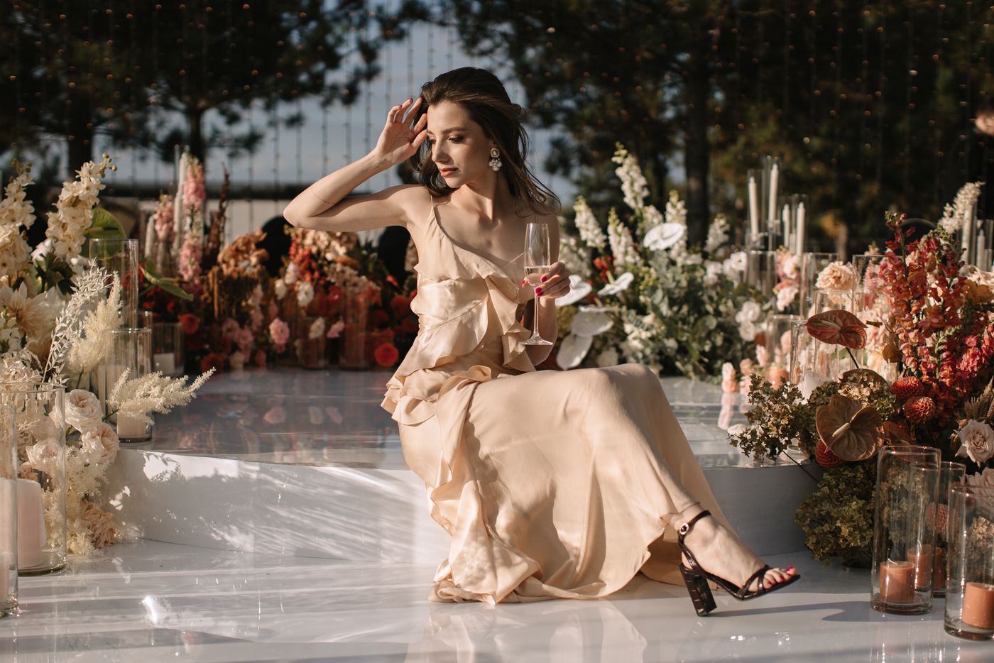 Elegant wedding scene with person in flowing peach dress posed among floral decorations.