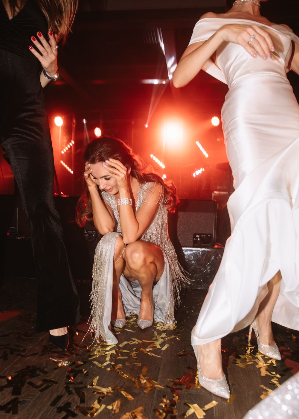 Wedding guests dancing energetically on a dance floor with red lighting and confetti.