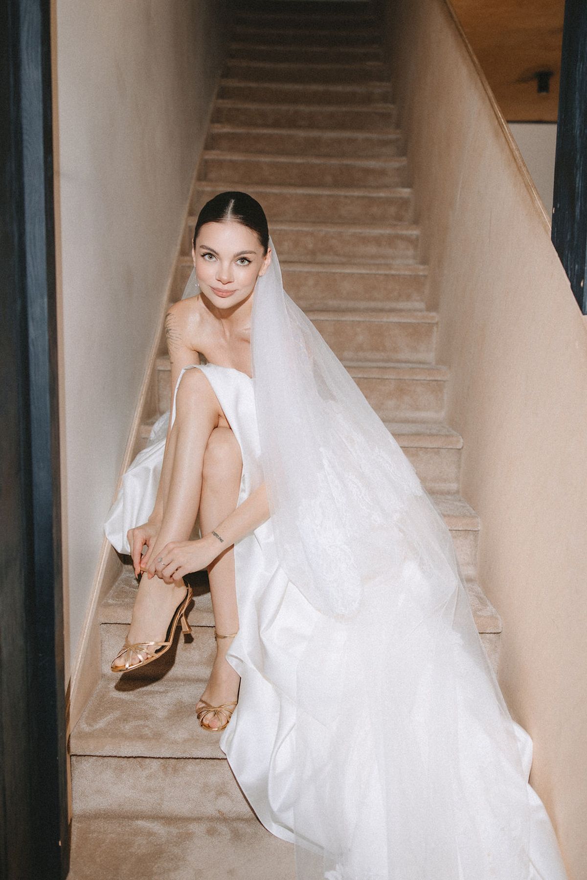 A bride in a flowing white wedding dress sits gracefully on elegant stone stairs.