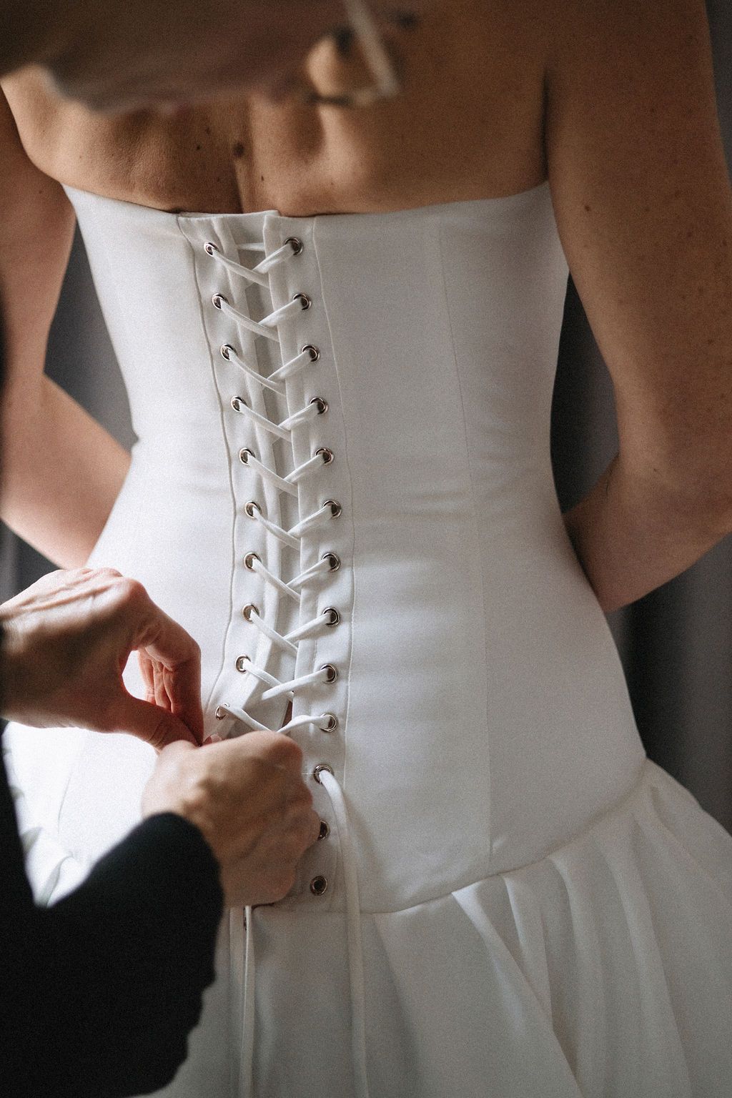 A series of photos showing the intricate lacing detail on the back of a white wedding dress being tied up.