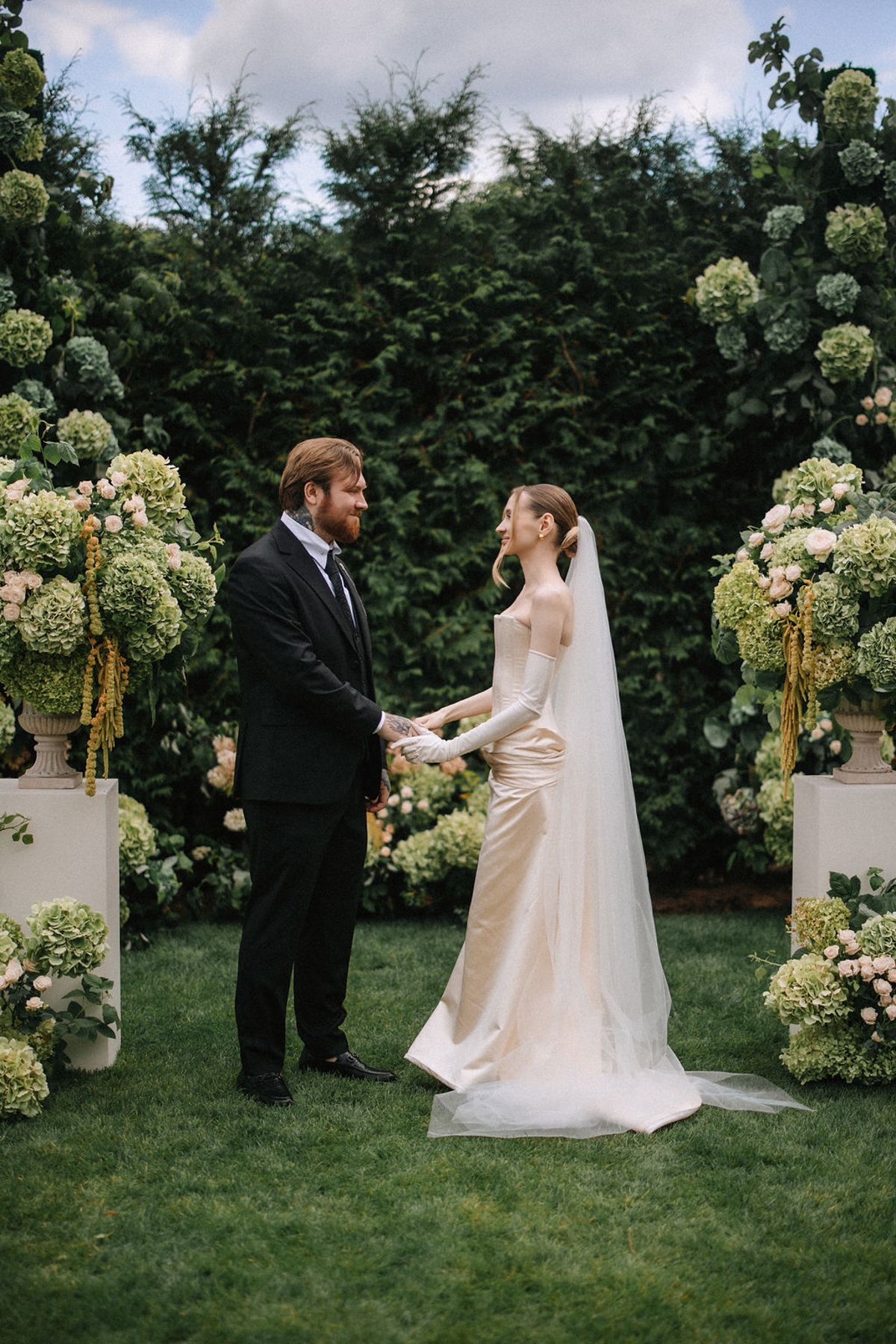 A couple shares a joyful moment during their garden wedding ceremony surrounded by elegant white floral arrangements.