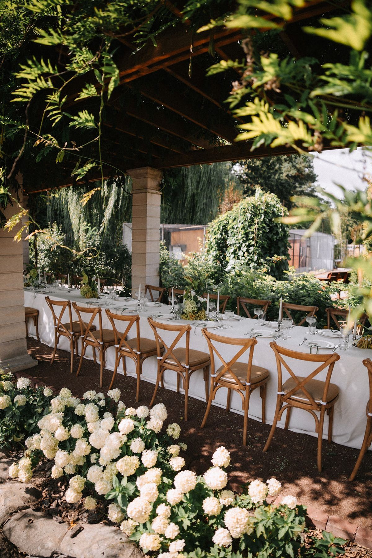 Elegant outdoor wedding reception setup with rustic wooden chairs and lush floral arrangements under a covered patio.