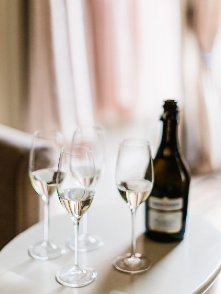 Three champagne flutes filled with sparkling wine sit beside an unopened bottle on a white surface.