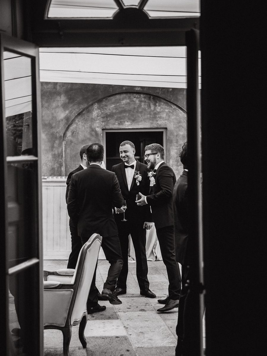 Black and white photograph of three men in formal attire having a conversation in a doorway.