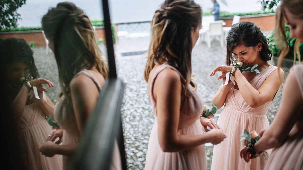 Bridesmaids in soft pink dresses gather together during wedding preparations.