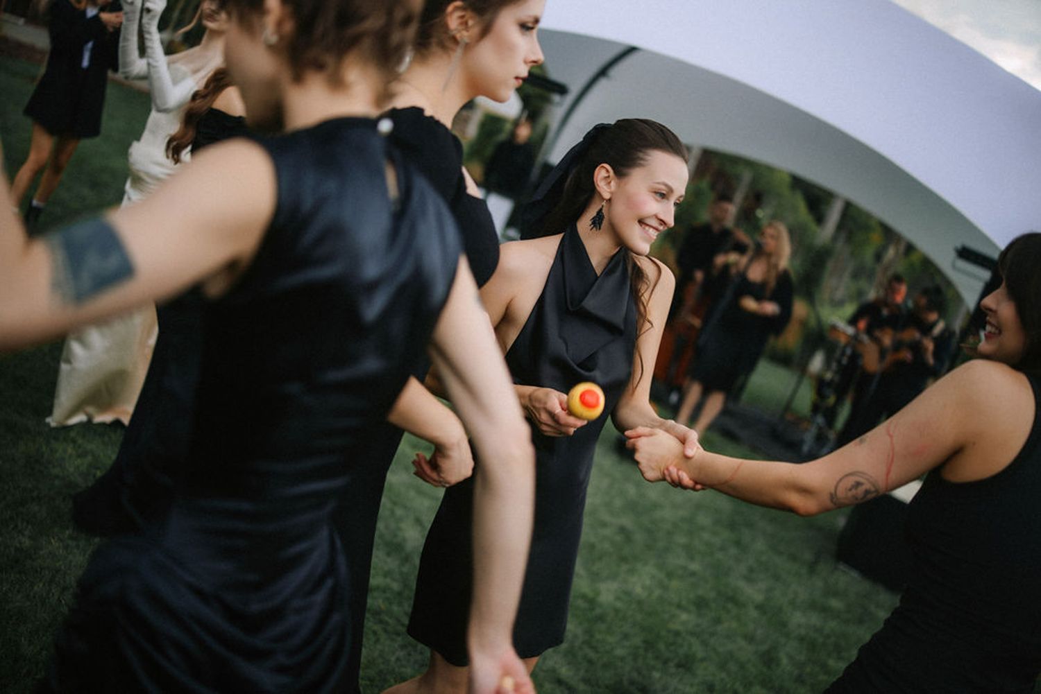 Wedding guests dance and celebrate on a grassy outdoor dance floor during an evening reception.