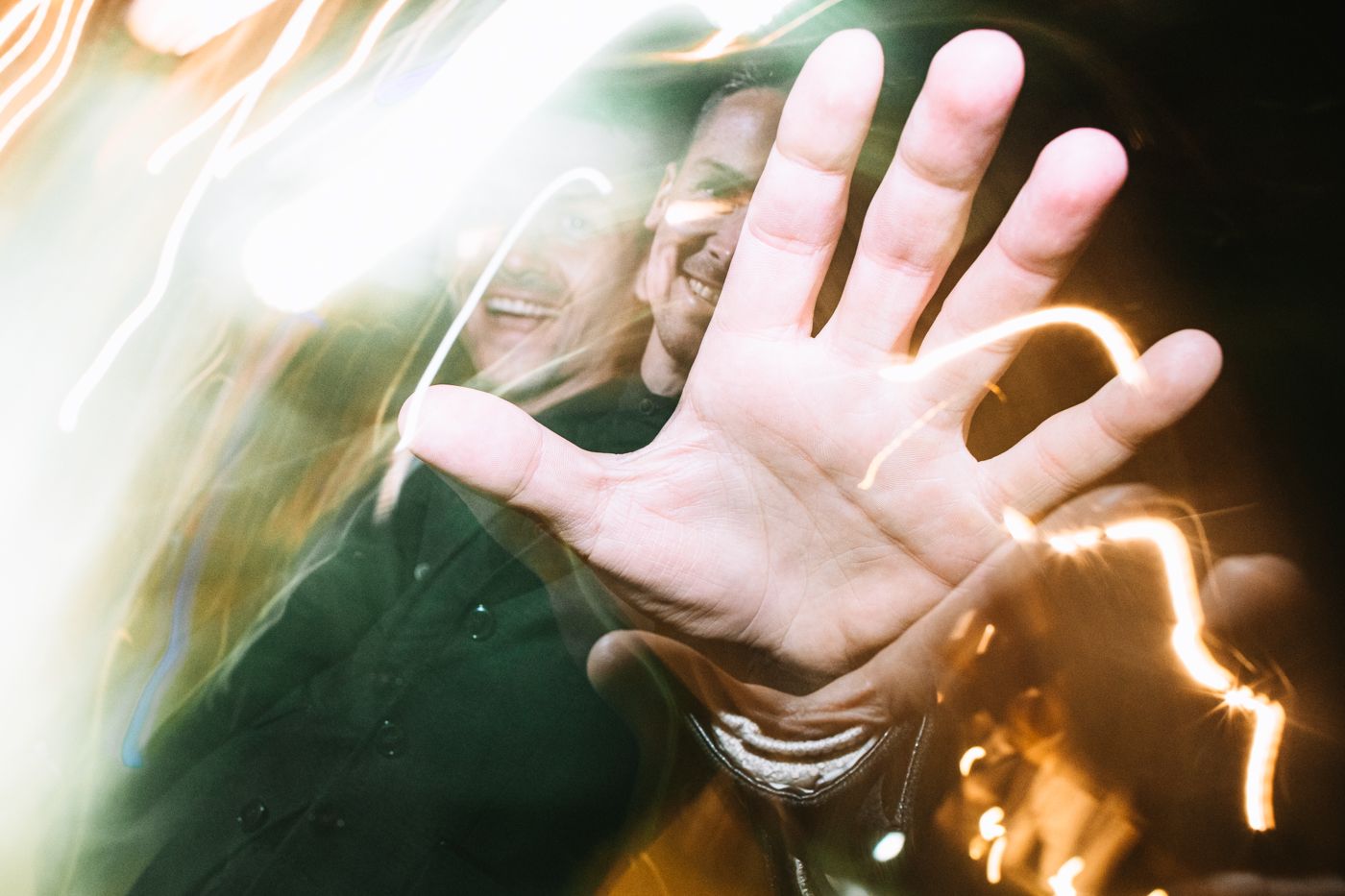 A hand reaches out against a blurred background with orange and white light streaks creating an ethereal effect.