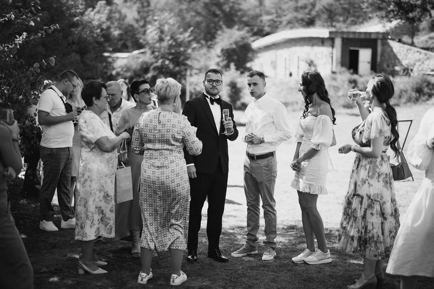 A black and white photo of guests mingling at an outdoor garden party or wedding reception.
