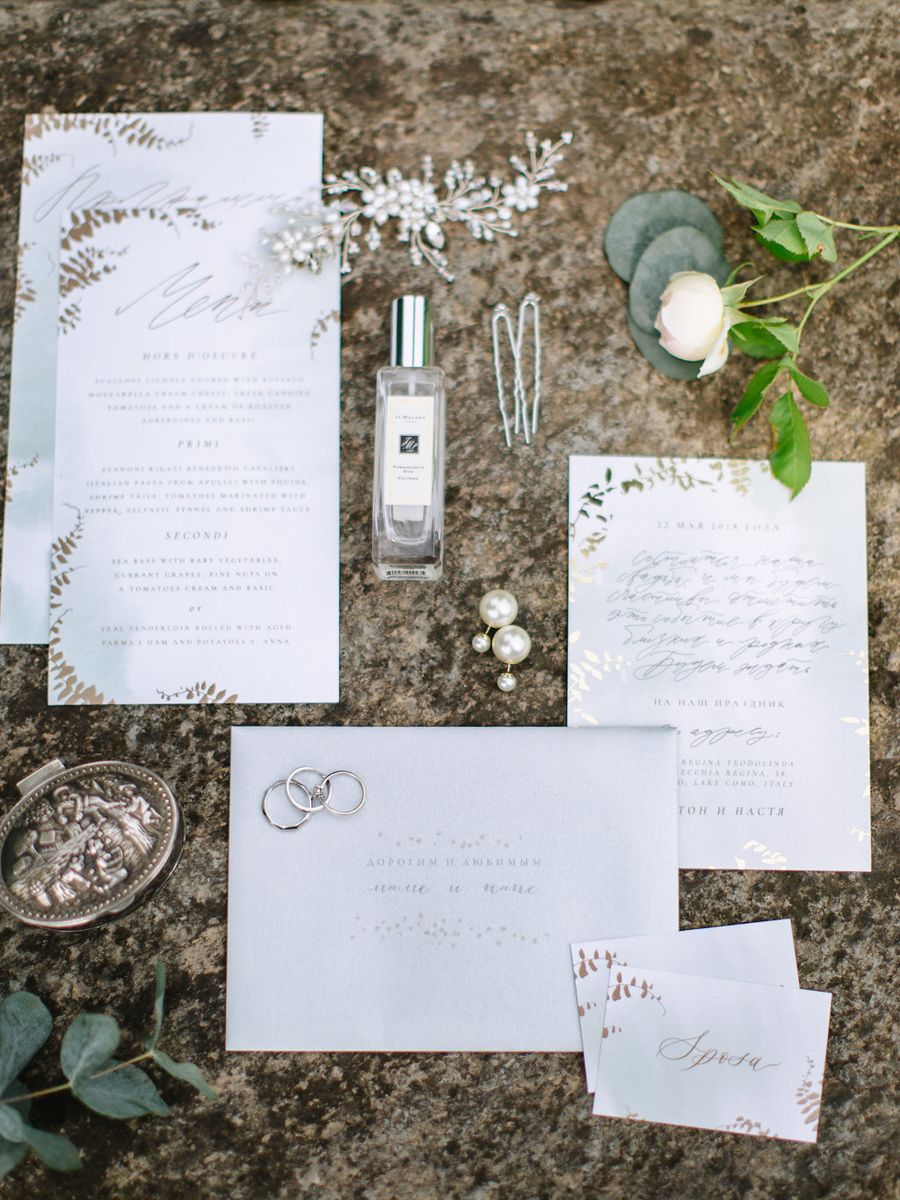 Elegant wedding invitation suite with white stationery and calligraphy laid out on a stone surface with greenery accents.