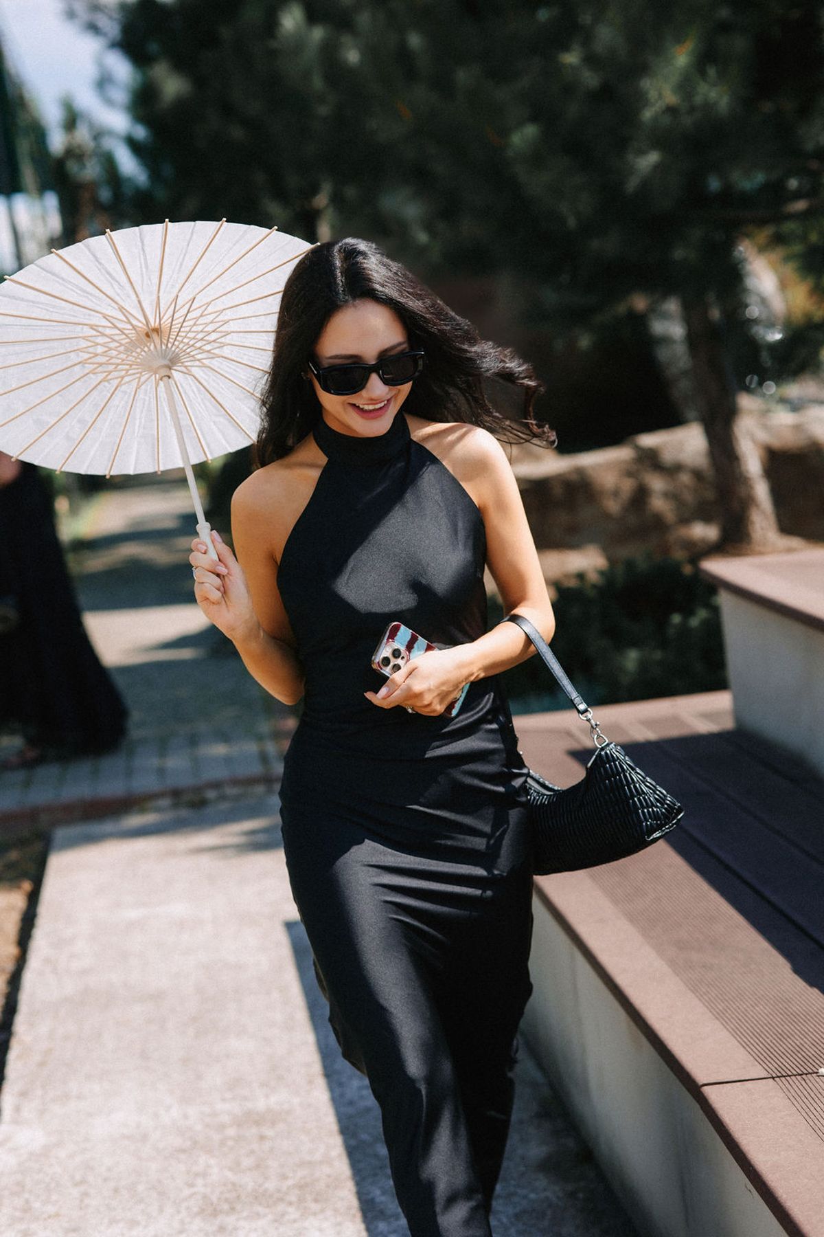 A woman in black activewear poses with a white decorative parasol in an outdoor setting with sunlit steps.