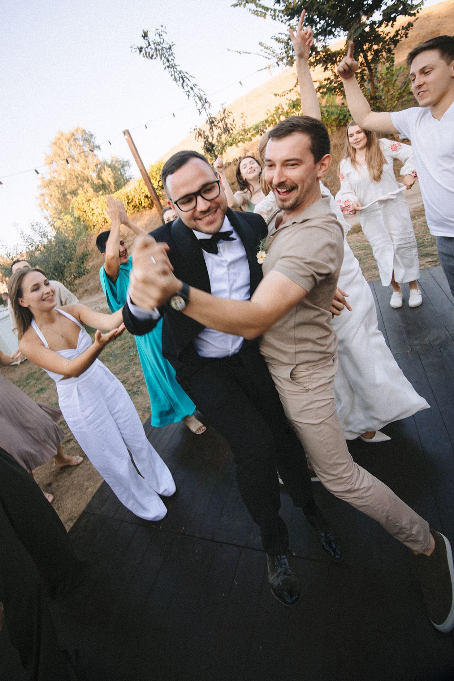 A fun wedding party jumps together in coordinated outfits during an outdoor photo session at sunset.