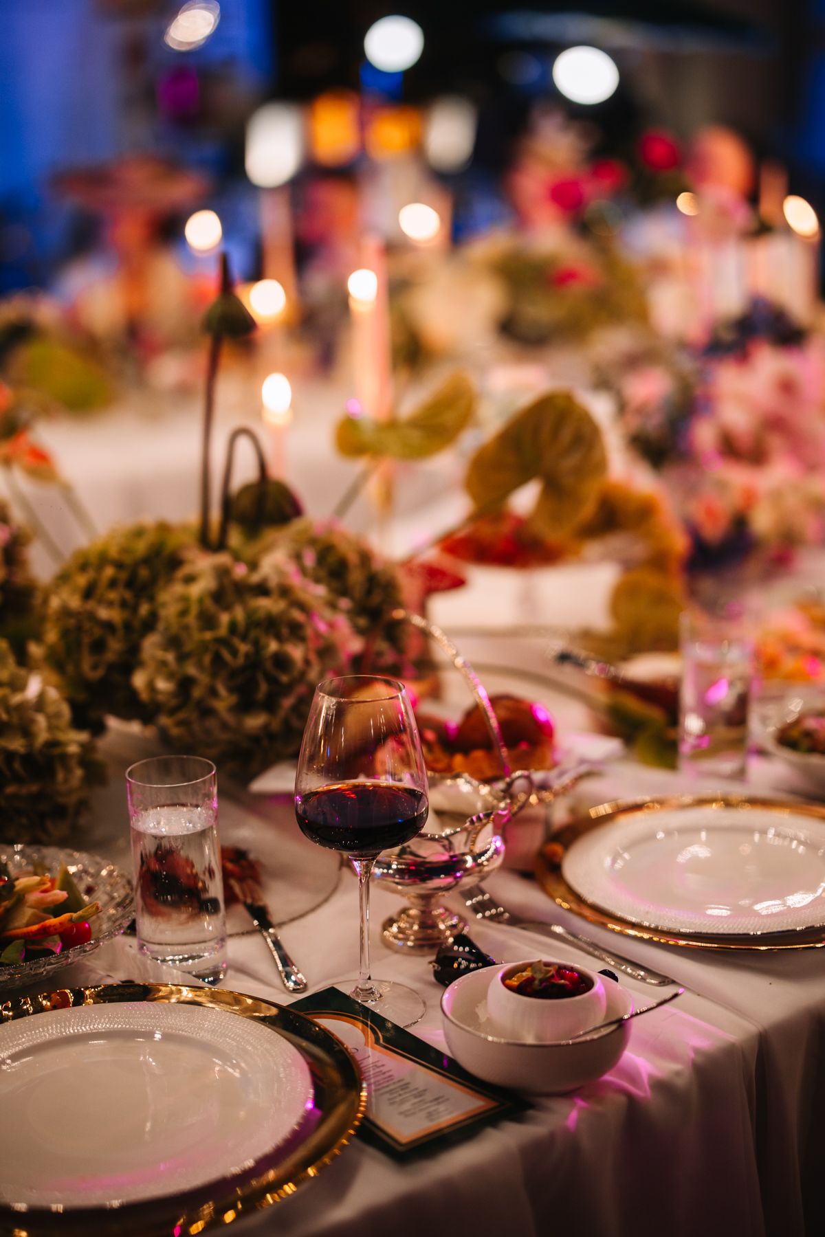 Elegant table setting at wedding reception with wine glasses, white plates and pink floral decorations in warm lighting.