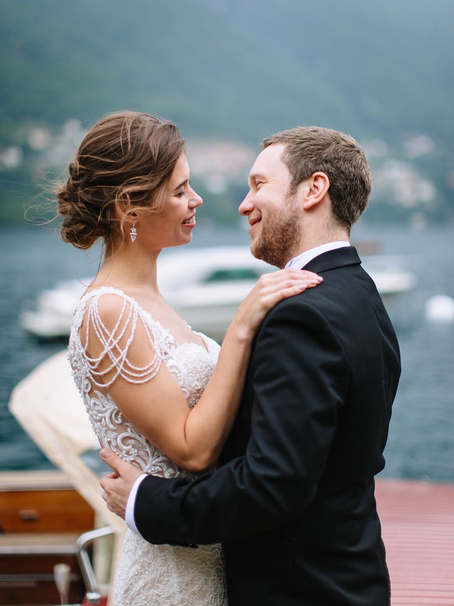 A couple shares a romantic moment on a boat with a scenic lake and mountains in the background.
