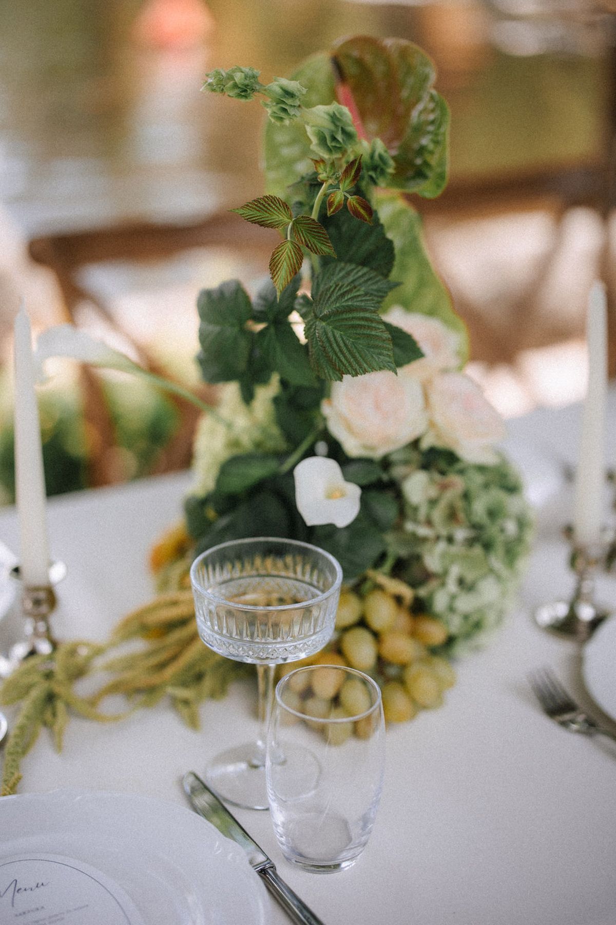 Elegant table setting with champagne glass and white floral centerpiece featuring fresh greenery and hydrangeas.