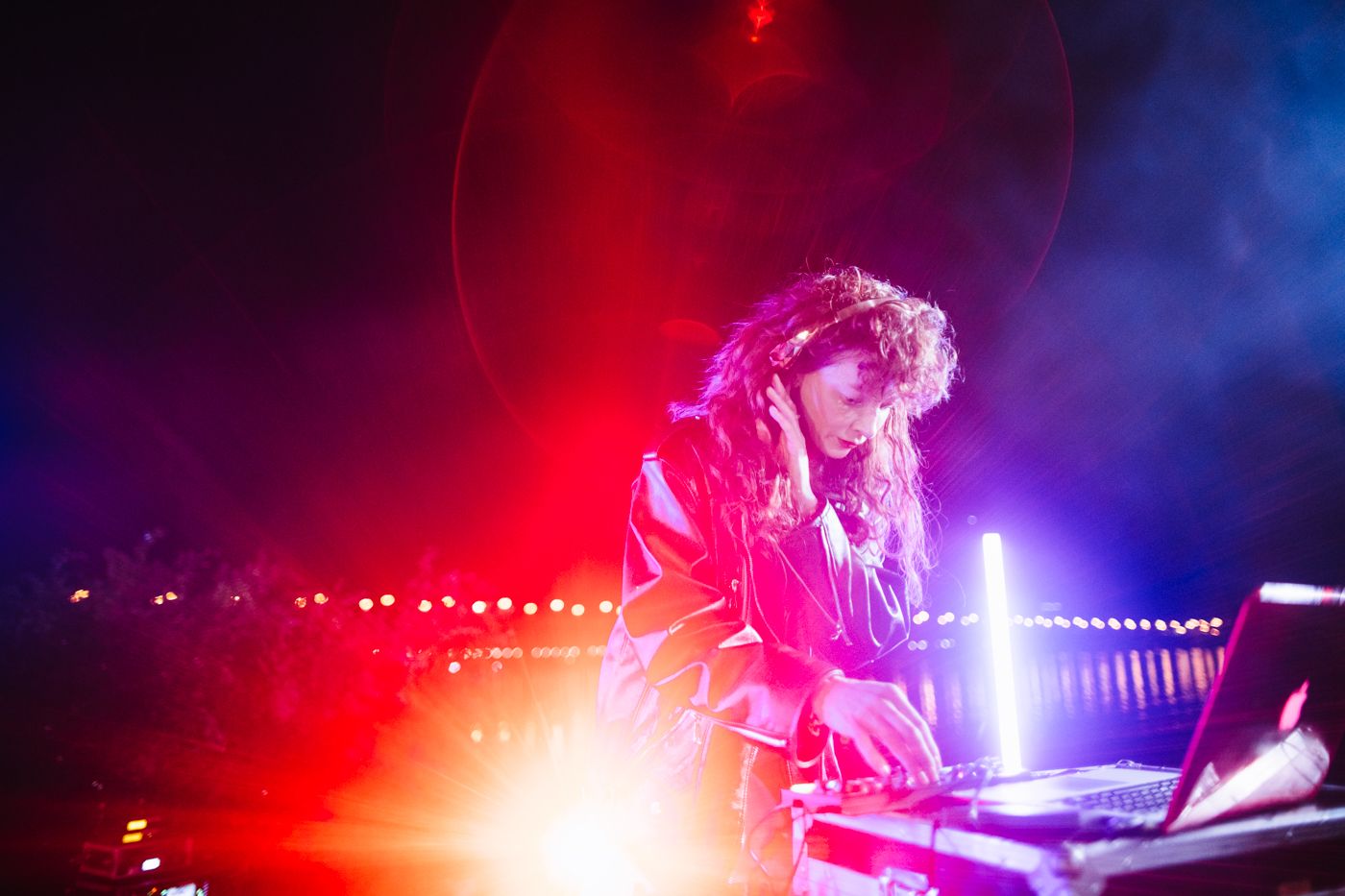 DJ performs at a turntable under vibrant red and pink stage lighting at a nightclub event.