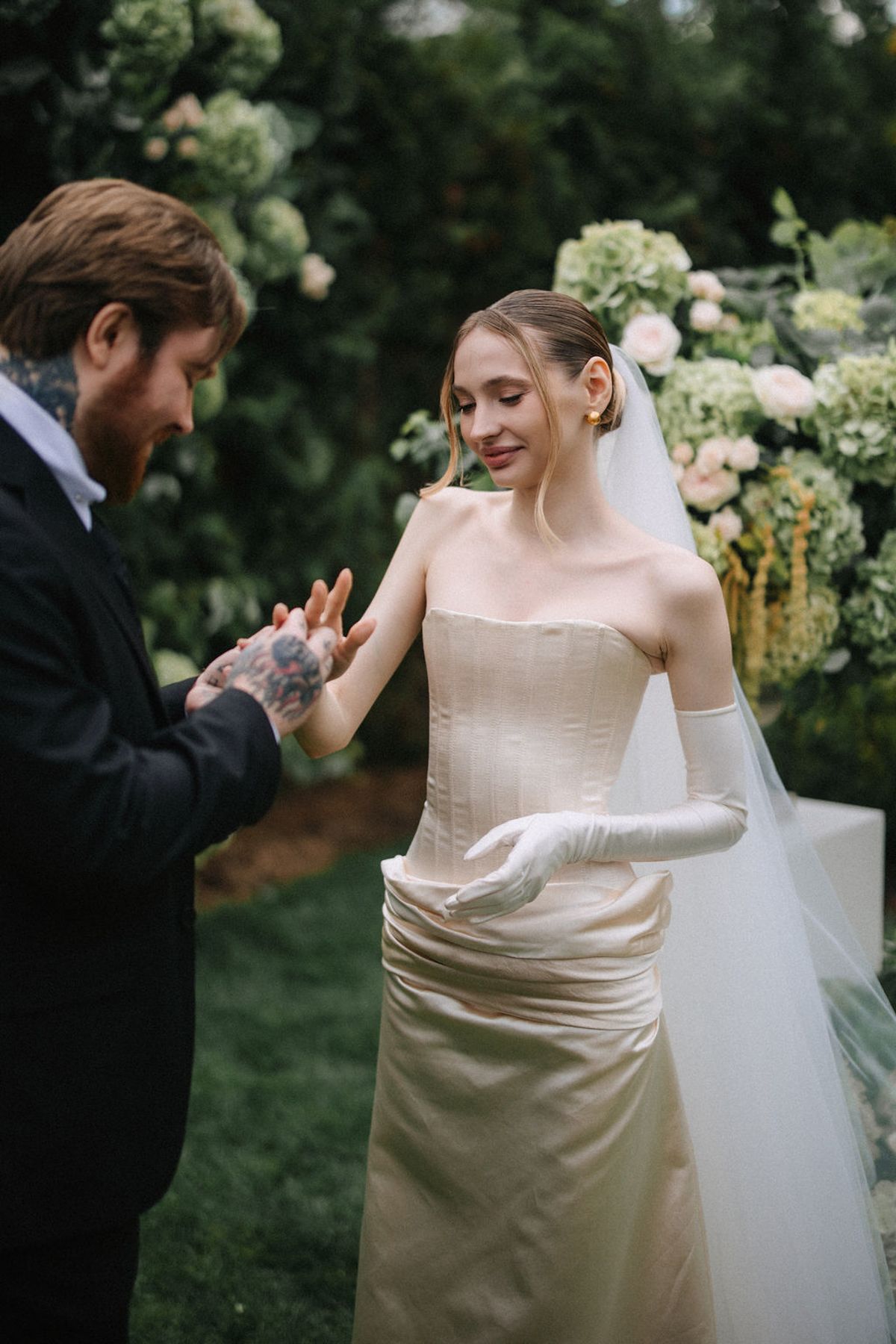 A romantic wedding moment captured in a garden setting with white flowers and greenery in the background.