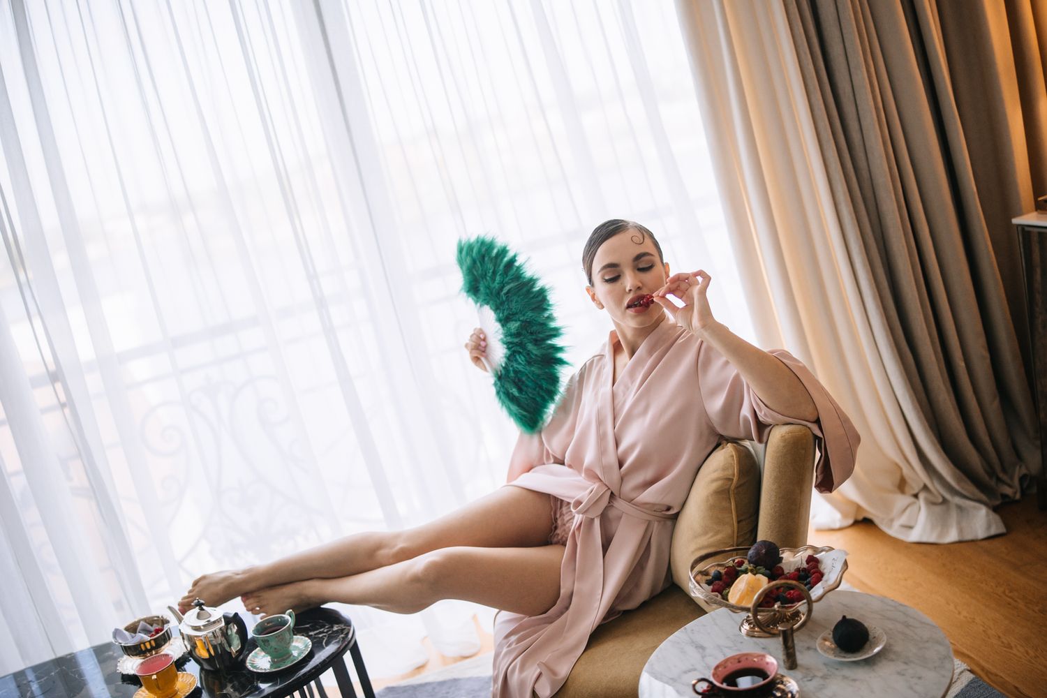 Professional cleaner in pink uniform dusts surfaces in a luxurious hotel room with natural lighting.