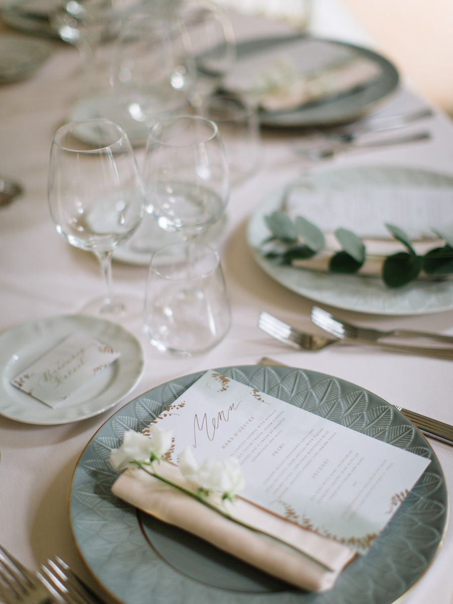 Elegant place settings at a wedding reception with sage green plates and white menus on a neutral tablecloth.
