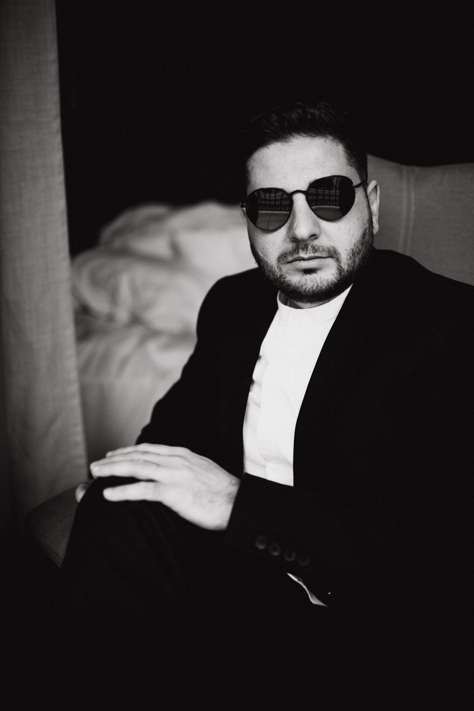 Monochrome portrait of person in black jacket and sunglasses against dark background.