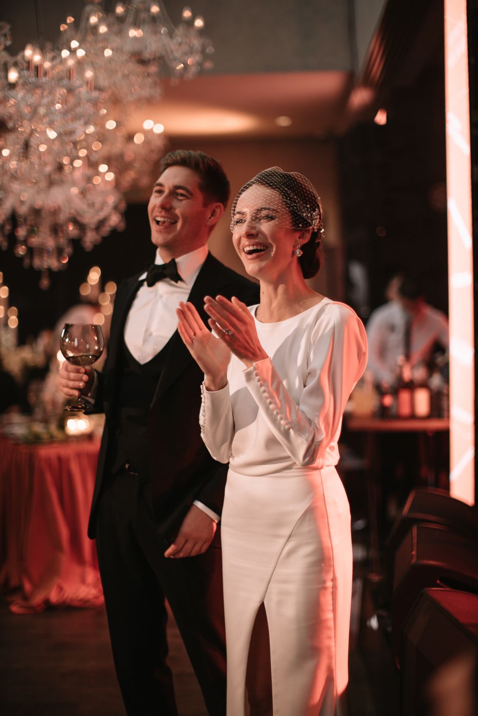 Wedding celebration under crystal chandeliers with joyful moments captured in warm lighting.