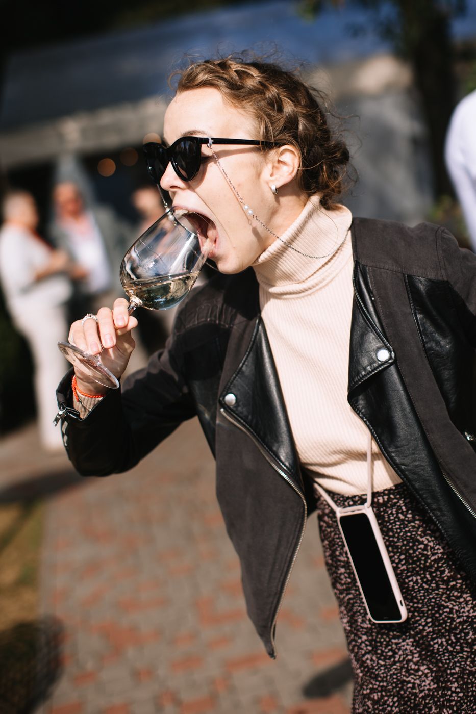 Person in black leather jacket and dress drinking from a glass at a party.